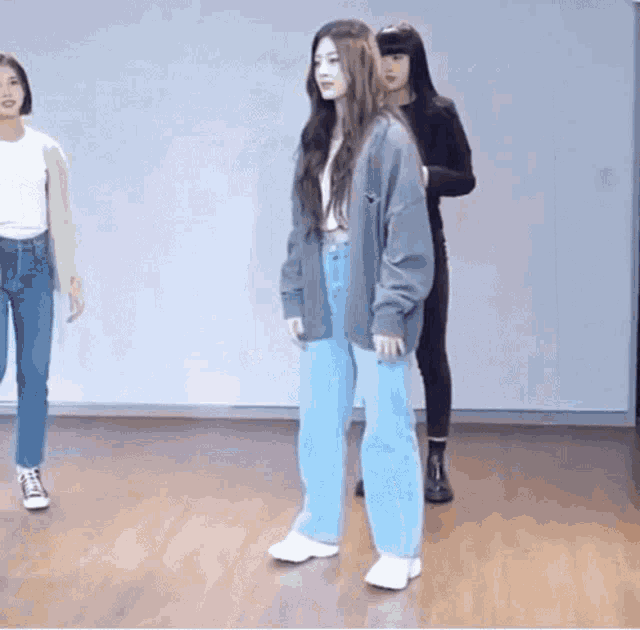 a woman in a gray cardigan and blue jeans is standing on a wooden floor in a dance studio .