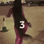a woman is walking down a street with a cone in the background and the number three on her back .