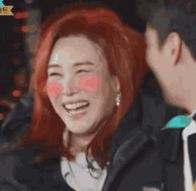 a woman with red hair is laughing with a man in the background