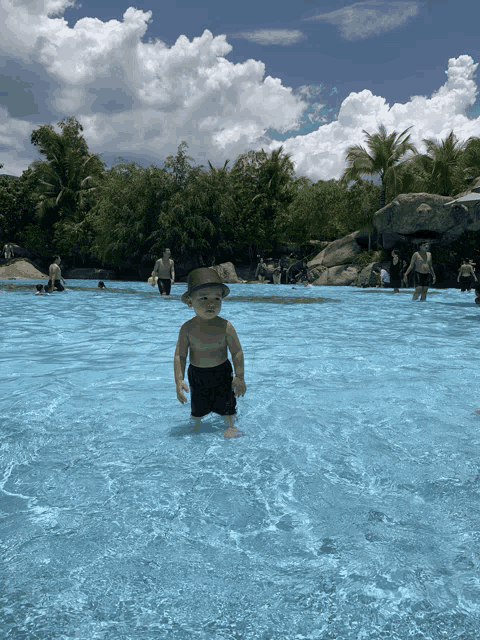a baby wearing a hat stands in a pool