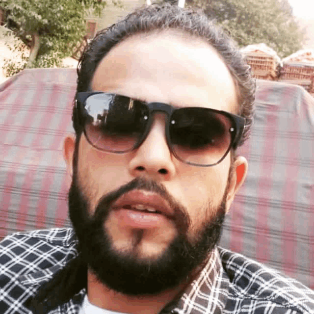 a man with a beard and sunglasses looks at the camera
