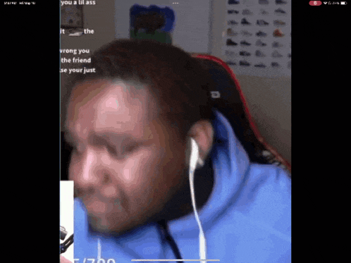 a man wearing ear buds is sitting in front of a screen that says ' you a lil ass '