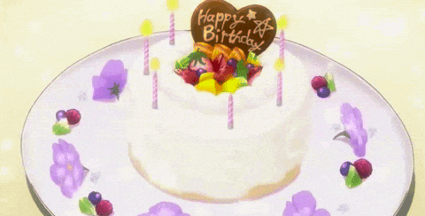 a birthday cake with candles and flowers on a plate with the words happy birthday written on it