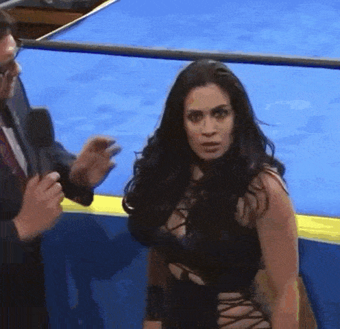 a woman in a black dress is standing in a wrestling ring next to a man in a suit .