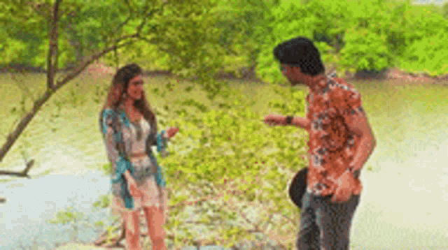 a man and a woman are standing next to each other in front of a body of water .