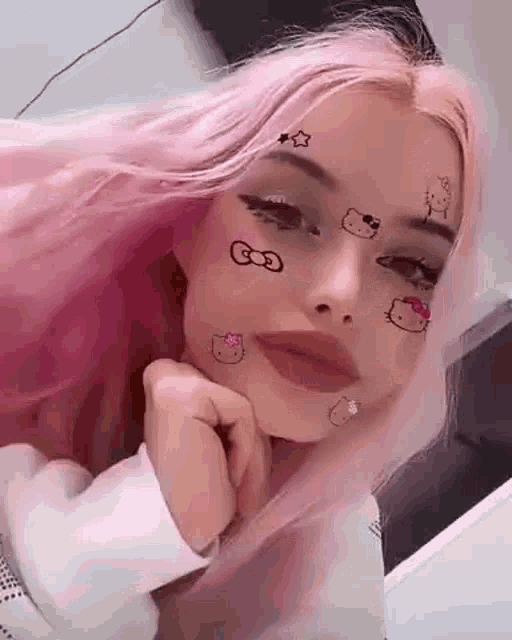 a girl with pink hair and hello kitty stickers on her face is looking at the camera .