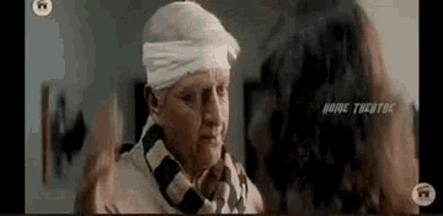 a man with a bandage on his head is talking to a woman in a room .