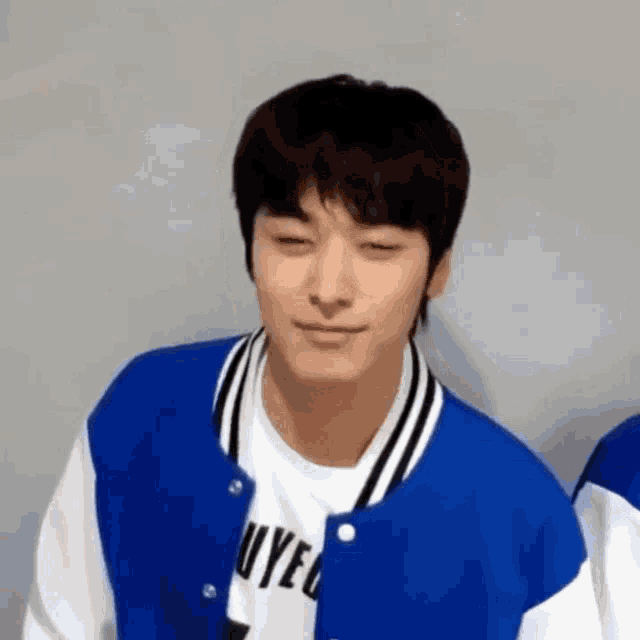 a young man wearing a blue and white baseball jacket and a white t-shirt .