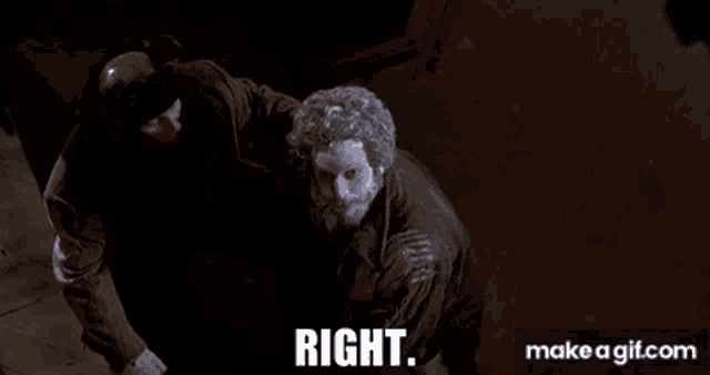 two men are standing next to each other in a dark room and one of them is wearing a mask .