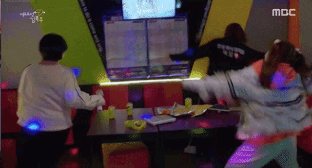 two girls are playing a video game in a room that says mbc on the screen