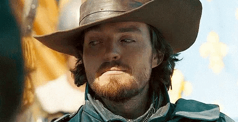 a man with a beard is wearing a cowboy hat and looking at the camera .