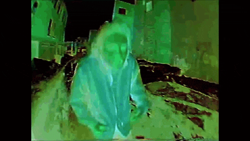a person in a green hoodie is standing in front of a building .