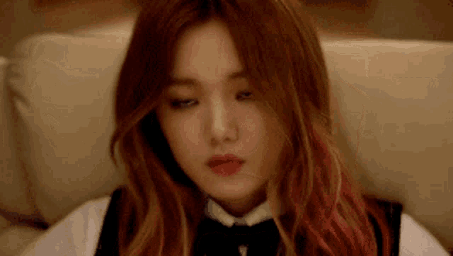 a woman with red hair is sitting on a couch with her eyes closed and making a funny face .