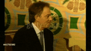 a man in a suit and tie is standing in front of a wall with a clock on it .
