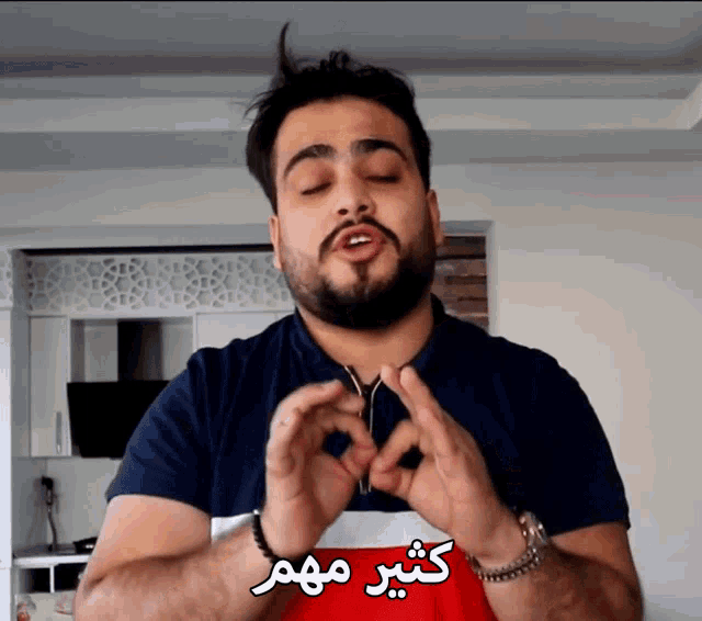 a man with a beard is making a heart shape with his hands in front of a sign that says " كثير مهم "