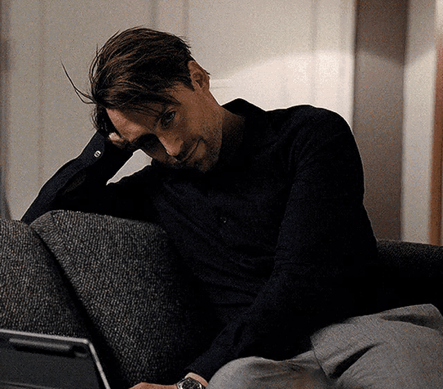 a man is sitting on a couch looking at a laptop computer