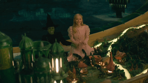 a woman in a pink dress is sitting next to a witch
