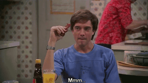 a man in a blue shirt is eating a piece of bacon and says hmm ba-con