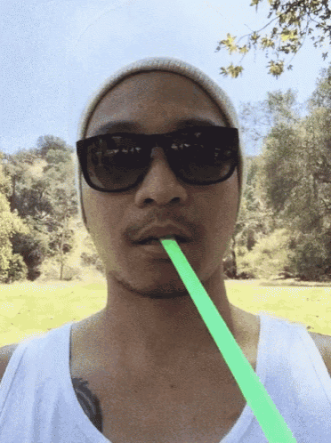 a man wearing sunglasses and a beanie is drinking a green straw