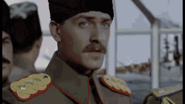 a man in a military uniform with a mustache is standing in front of a group of men .