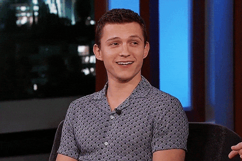 a young man is sitting in a chair and smiling while wearing a polka dot shirt .