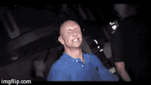 a bald man in a blue shirt is making a funny face while dancing in a club .