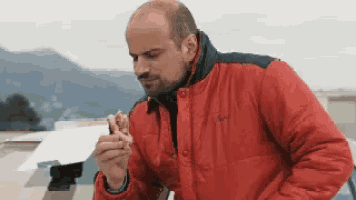 a man in a red jacket is eating a piece of pizza