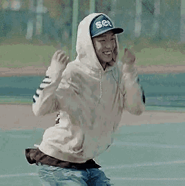 a man wearing a hoodie and a baseball cap is dancing on a tennis court .