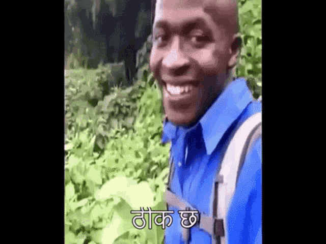 a man wearing a blue shirt and a backpack is smiling while standing in a field .
