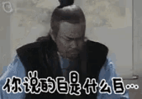a man with a bun on his head is sitting in front of a wall with chinese writing on it .