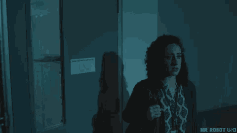 a man is standing in a dark room looking out of a window .