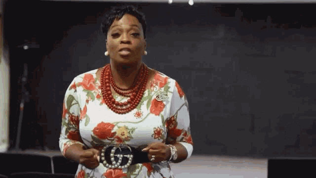 a woman wearing a floral dress and a belt with a g on it .