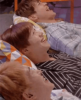 a group of young men are laying on a bed laughing