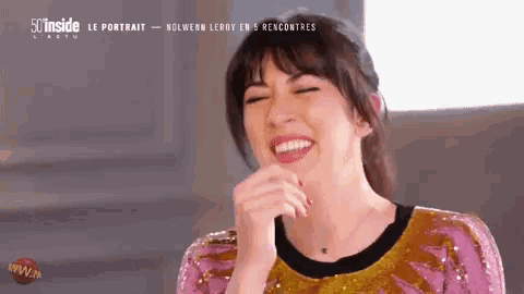 a woman in a pink and gold dress is laughing with her hand on her face .