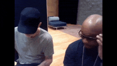 a bald man wearing sunglasses and a hat sits next to a bald man wearing a hat