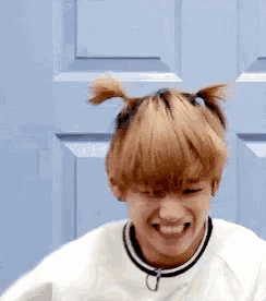 a young man with pigtails on his head is smiling and making a funny face .