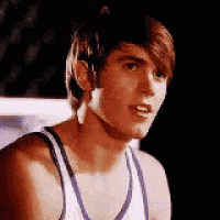 a young man wearing a white tank top is looking at the camera and smiling .