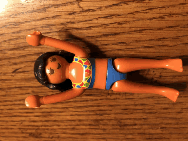 a playmobil doll is laying on its back on a wooden surface