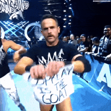 a wrestler is holding a sign that says ' i am the goat '