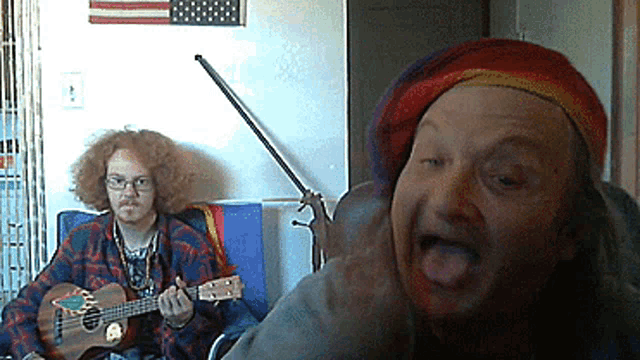 a man with curly hair is playing a guitar while another man looks on