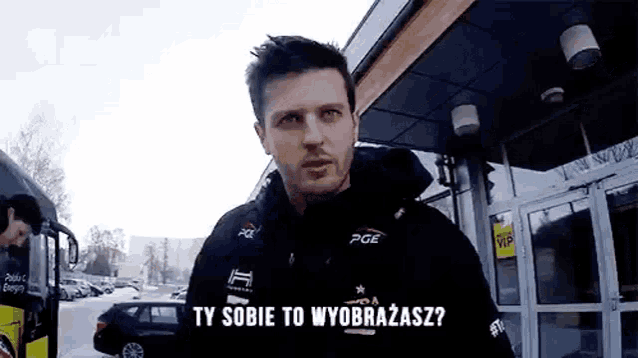 a man in a black jacket is standing in front of a building and talking .