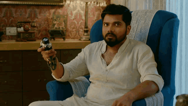 a man in a white shirt is sitting in a chair holding a gun