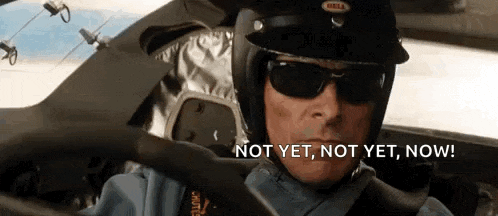 a man wearing a helmet and sunglasses is driving a car and says `` not yet , not yet , now ! ''