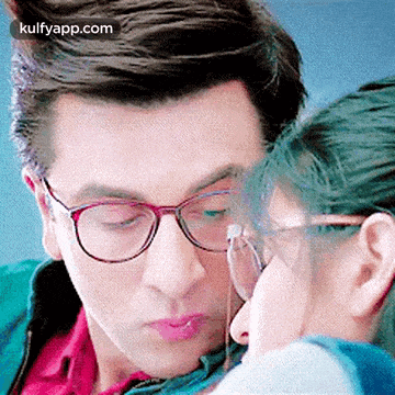 a man wearing glasses is kissing a woman 's forehead .