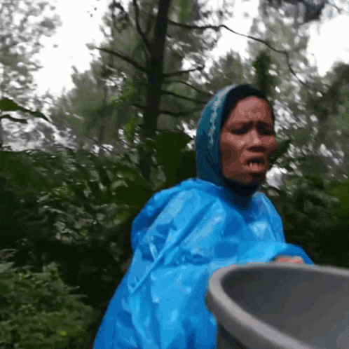 a woman in a blue raincoat holds a black bucket