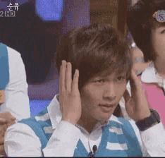 a man in a blue vest is covering his ears in front of a 2hd sign