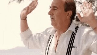 a man wearing a white shirt and suspenders is standing in front of a tree .