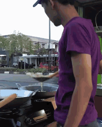 a man in a purple shirt is cooking food in a pan