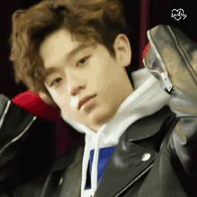 a young boy wearing a leather jacket and a hoodie is holding a red object .