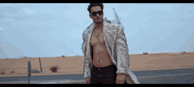 a shirtless man in a fur coat and sunglasses stands in the desert